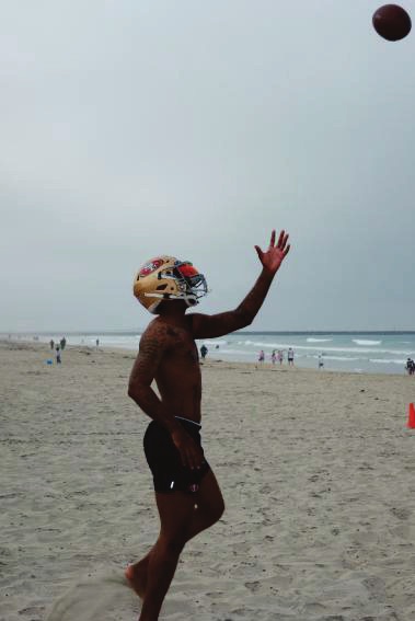 Love shirtless on a beach wearing a 49ers helmet catching a football